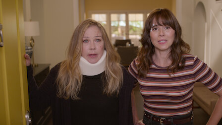 Christina Applegate, with a neck brace, and Linda Cardellini are surprised as they open the front door.